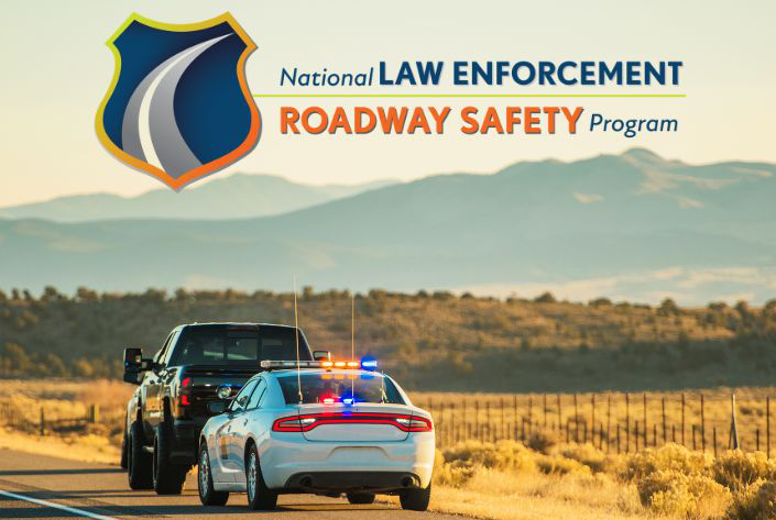 A police vehicle with activated lights stops a truck on a rural road at sunset, with mountains in the background and the 'National Law Enforcement Roadway Safety Program' logo displayed in the corner.