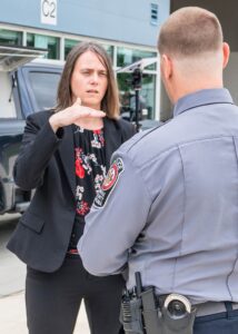 A woman gestures while speaking with a uniformed officer outside a building.
