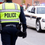 AQ policeman walking by a patrol car on the street.