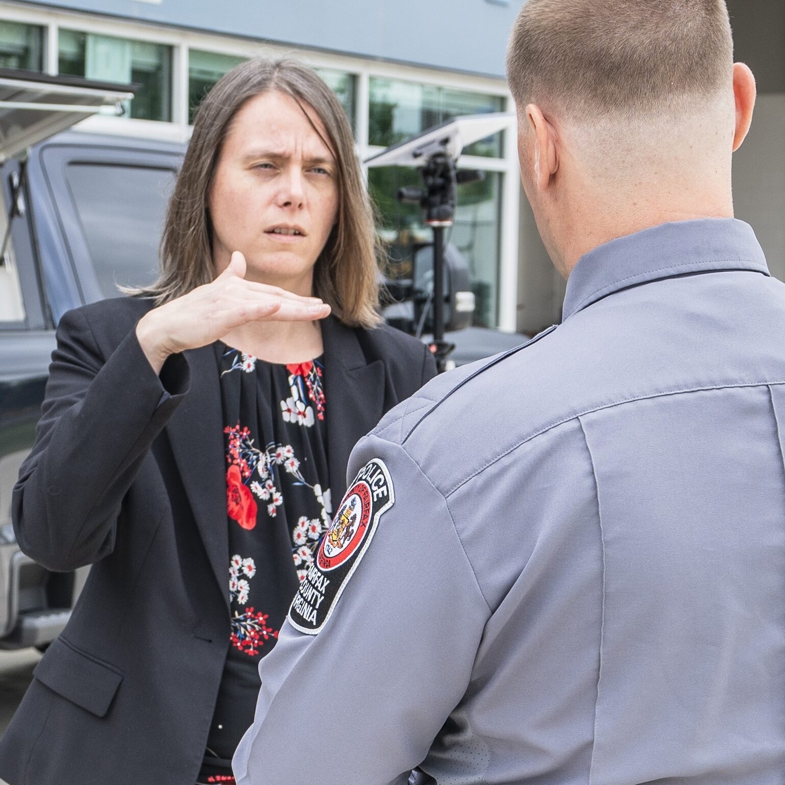 Consultant Discusses Operational Strategy with Law Enforcement Officer A woman gestures while speaking with a uniformed officer outside a building.