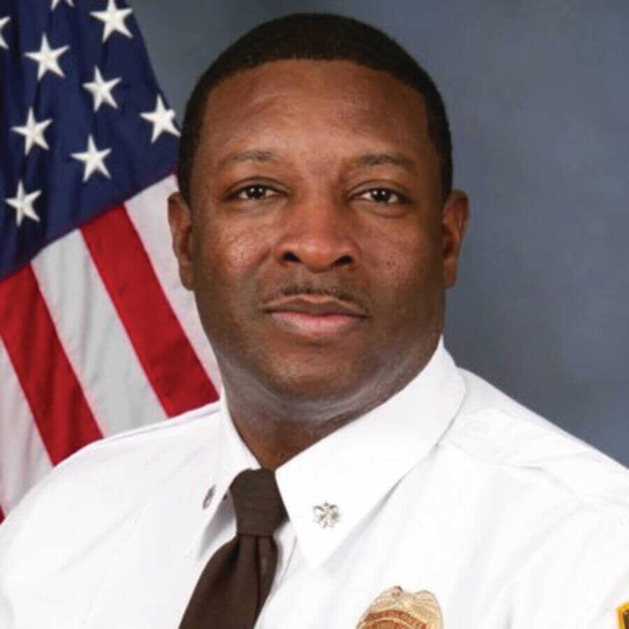 A uniformed man poses for a professional portrait in front of an American flag.