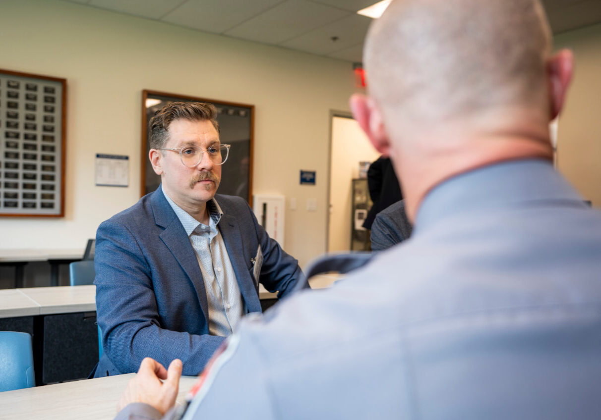Consultant Meeting with Officer to Discuss Data Quality A consultant listens attentively during a meeting with a uniformed officer in a classroom setting.