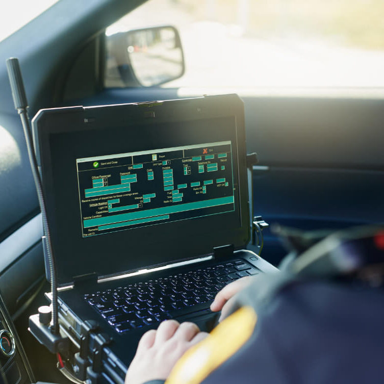 Police Officer Entering Incident Data on Mobile Computer A police officer uses a rugged laptop inside a patrol vehicle to enter or review data on a digital form.
