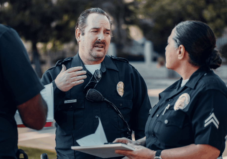 Police Officers Conducting Field Briefing with Notes Two uniformed police officers discuss information in an outdoor setting while reviewing a notepad.