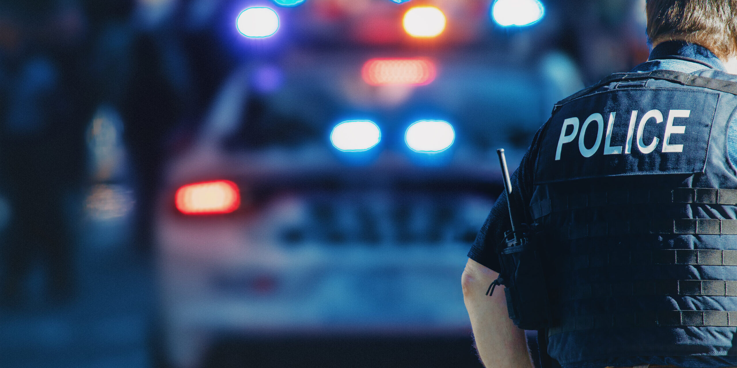 American,Policeman,And,Police,Car,In,The,Background