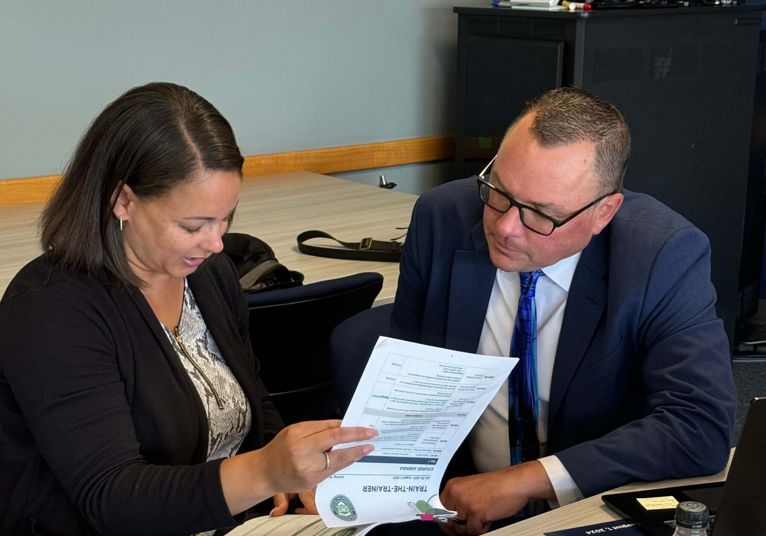 Colleagues Reviewing Wellness Program Materials A woman and a man review printed training materials together at a conference table.